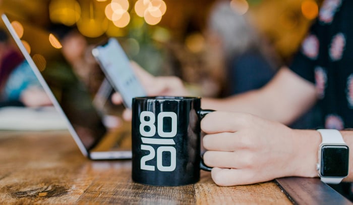 A man working on a laptop with a cup that says 80/20